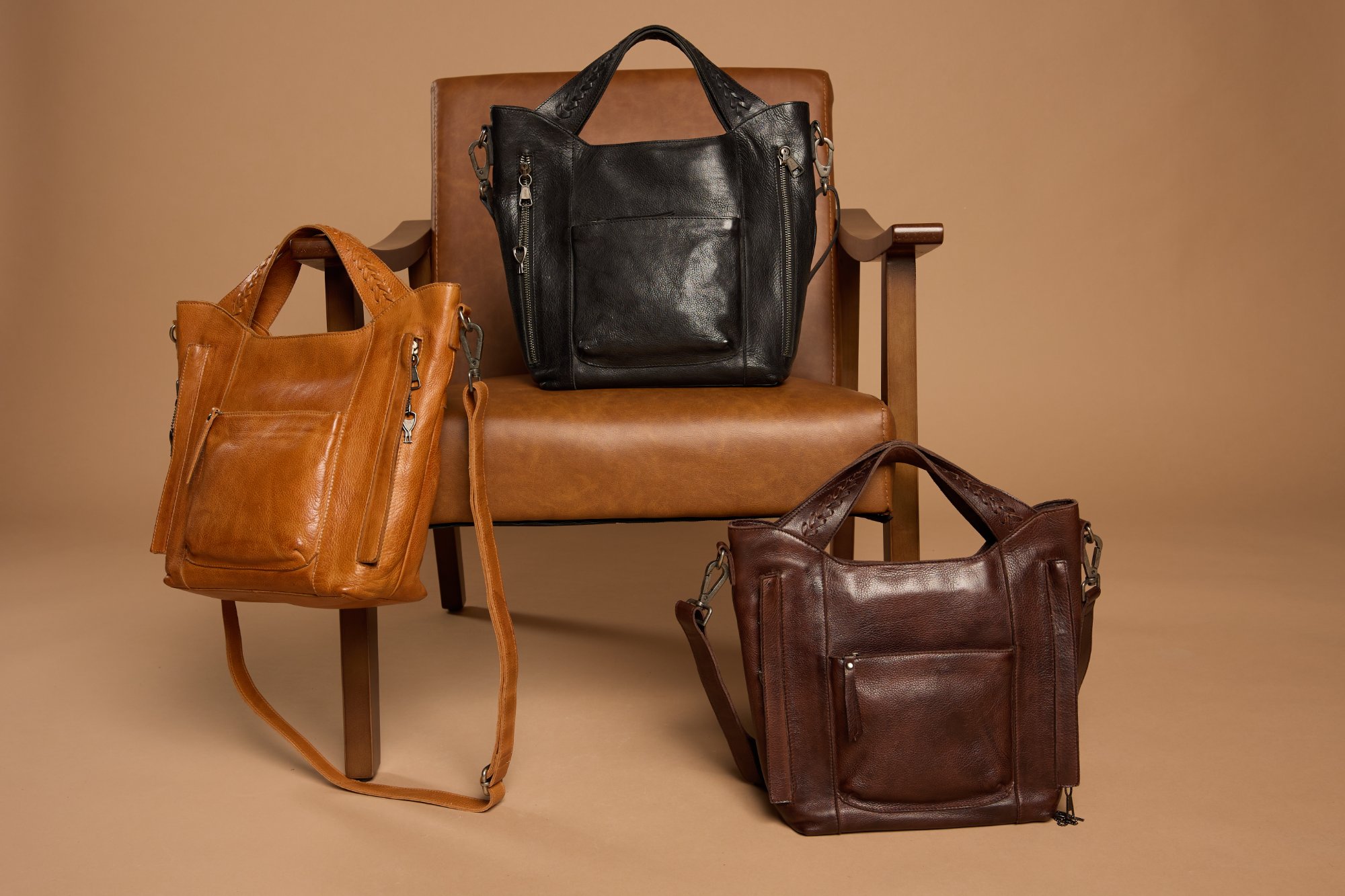 Three premium leather handbags in cognac, black, and brown styled on a leather chair